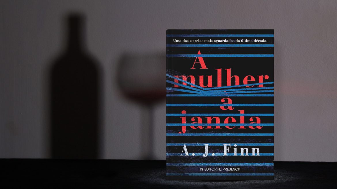 Livro "A mulher na janela" em cima de uma mesa e a sombra de uma garrafa de vinho e uma taça cheia atrás